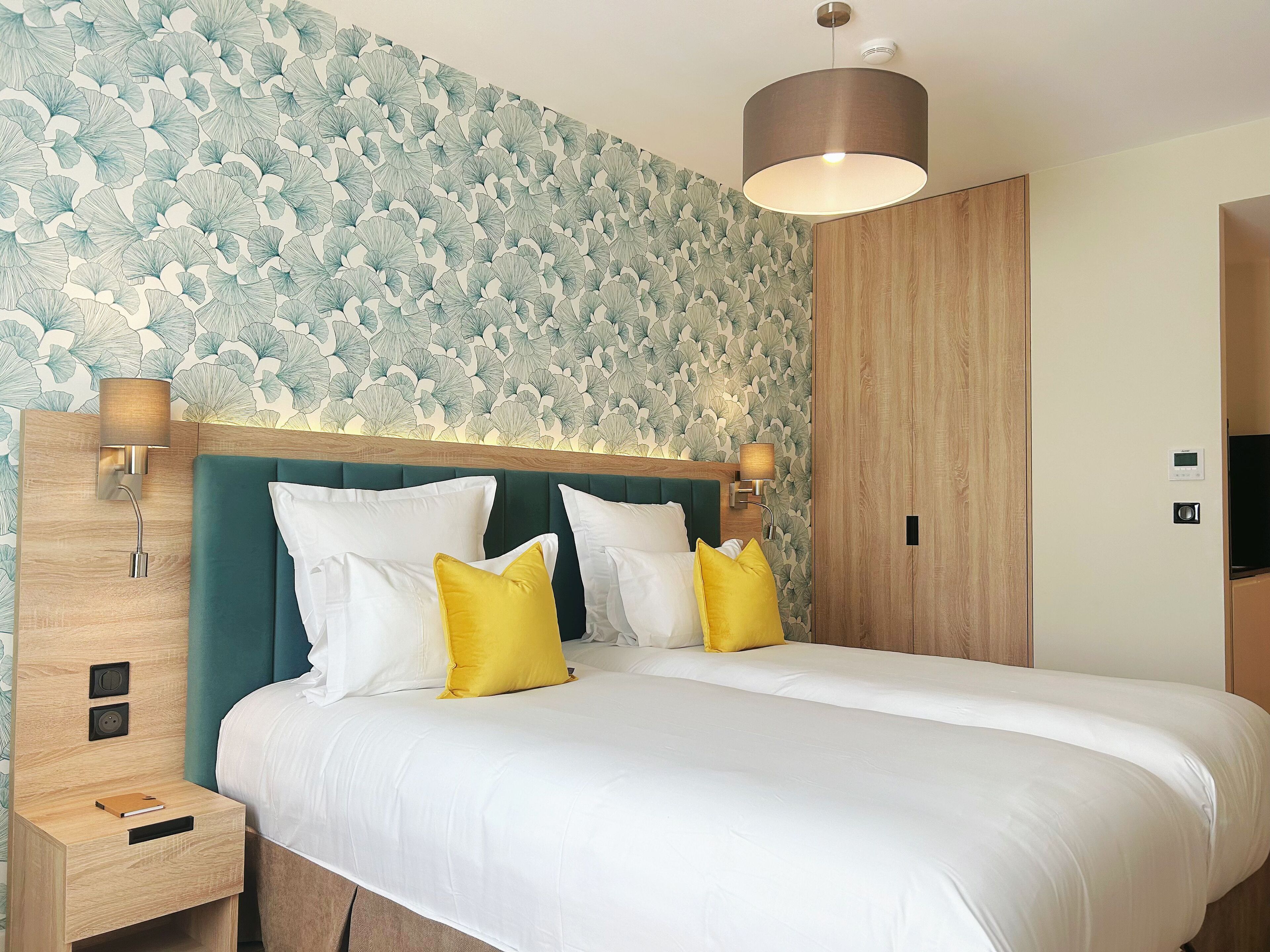 A hotel room with a large bed, two bedside tables, a wooden headboard, and a wall with a leafy pattern.