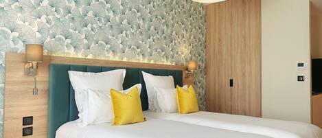 A hotel room with a large bed, two bedside tables, a wooden headboard, and a wall with a leafy pattern.