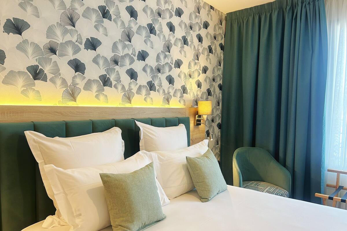 Ein Hotelzimmer mit Bett, grünem gepolsterten Kopfteil, weißer Bettwäsche und einem gemusterten Wandpapier.