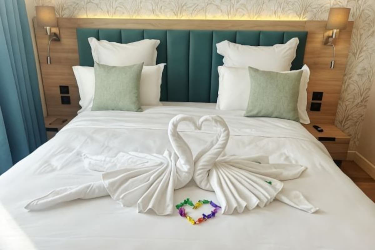 A hotel room with a large bed, two bedside tables, and a headboard with wall-mounted lamps.