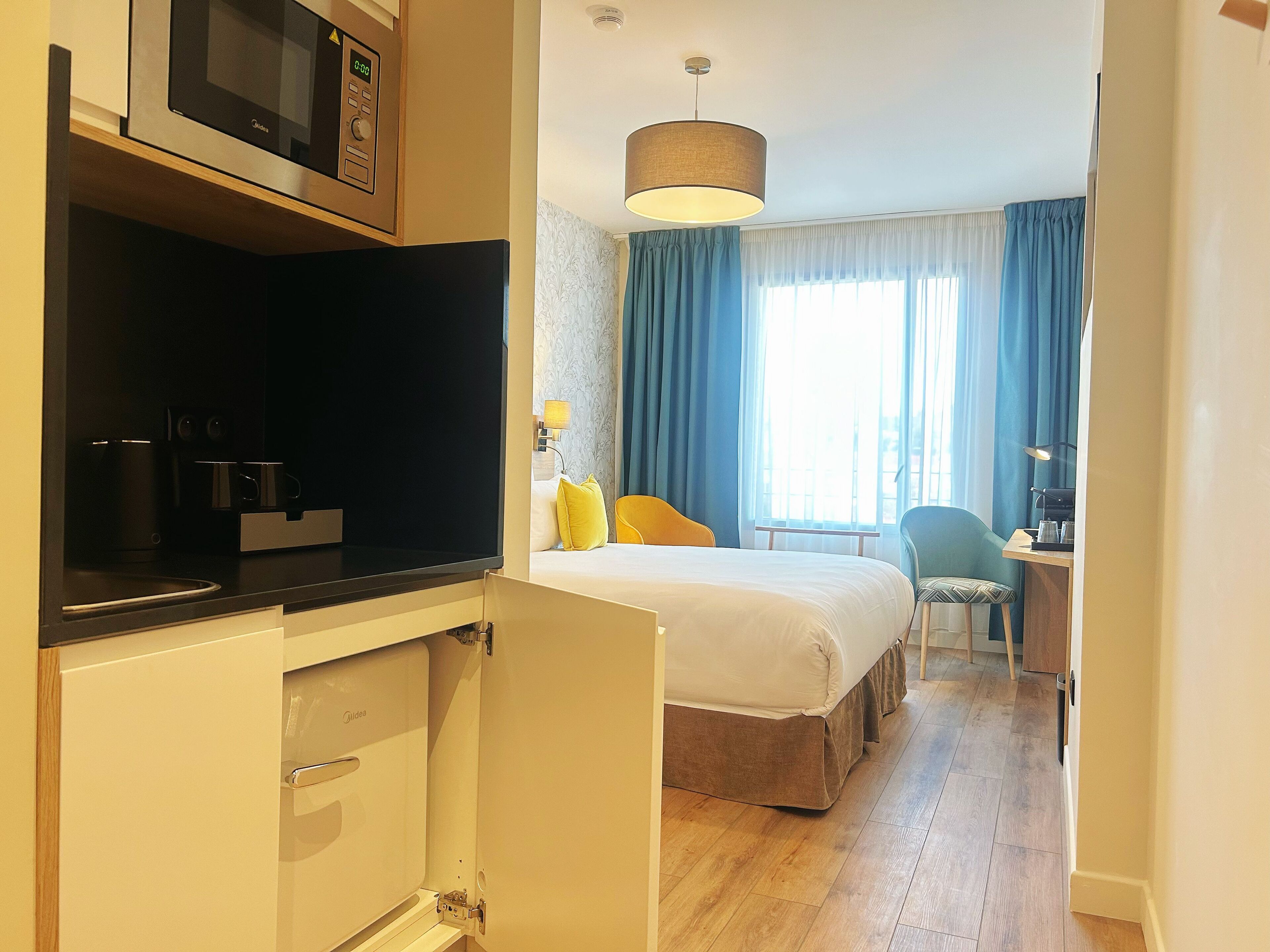 A hotel room with a bed, a desk, a chair, a microwave, and a coffee maker.