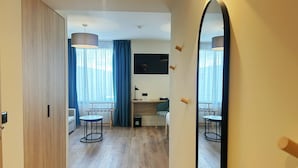 A modern hotel room with a wooden wardrobe, a desk with a chair, a small table, and a mirror. - Hôtel Oden Paris Ivry (Ivry-sur-Seine)