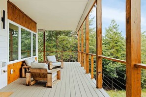 Una terraza de madera con dos sillas y una mesa, con vista a un área boscosa.