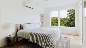 Une chambre à coucher comprenant un lit, une fenêtre, un appareil de climatisation et une table de chevet.