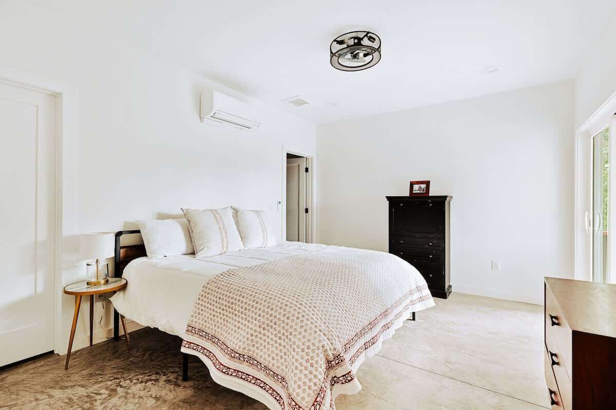 A bedroom with a bed, a bedside table, a dresser, and a ceiling light fixture.