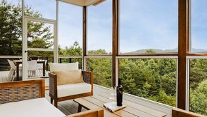 Un balcon spacieux avec une table en bois, une chaise rembourrée et une bouteille de vin.