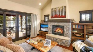 A cozy living room with a stone fireplace, a television, and a bookshelf.