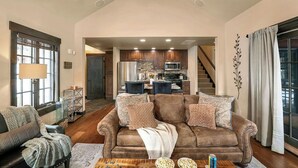 A spacious living room with a brown leather sofa, a wooden coffee table, and a dining area in the background.