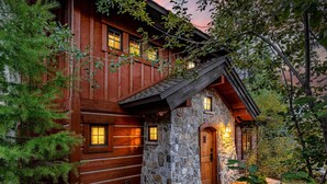 A rustic cabin with a stone entrance, wooden walls, and windows with warm lighting.