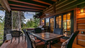 A covered outdoor patio with a wooden table and chairs, stone pillars, and a grill.