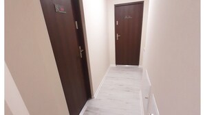 A narrow hallway with two wooden doors, white walls, and a tiled floor. - SouvenirAppart Sienkiewicza 3B (Bydgoszcz)