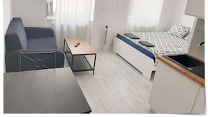A compact hotel room with a bed, a sofa, a small table, a TV mounted on the wall, and a kitchenette. - SouvenirAppart Sienkiewicza 3B (Bydgoszcz)