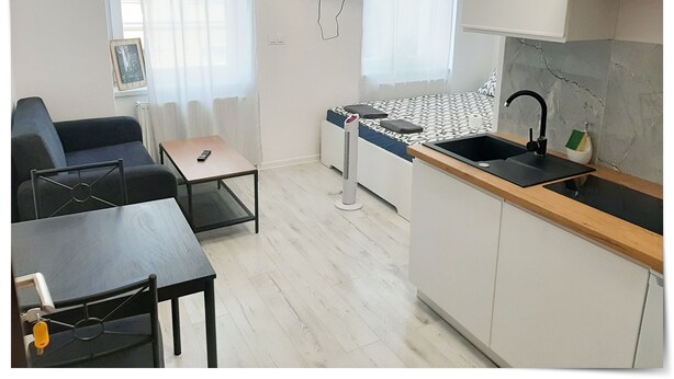 A compact living space with a kitchenette, a sofa, a small table, and a TV mounted on the wall. - SouvenirAppart Sienkiewicza 3B (Bydgoszcz)