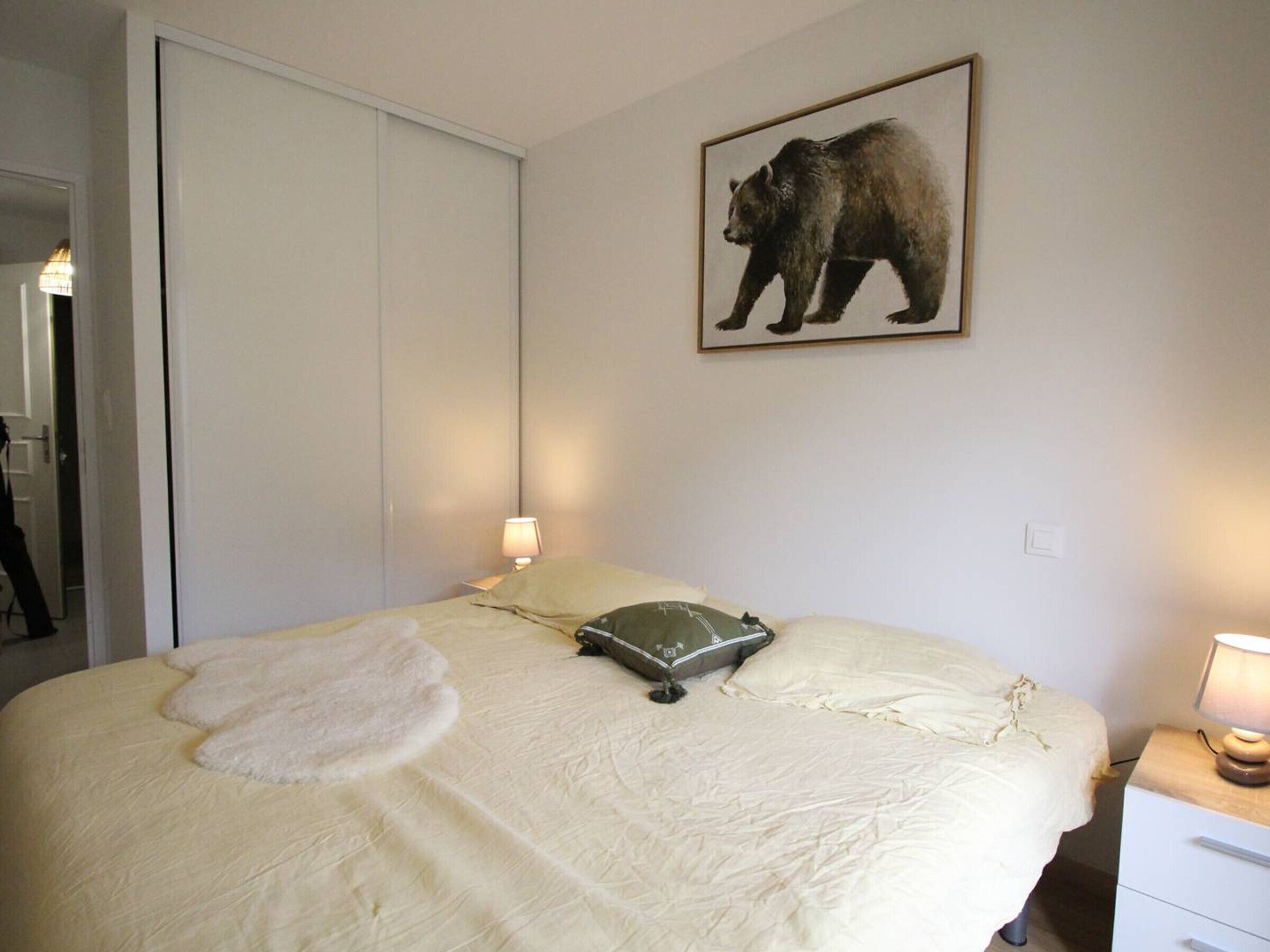Een slaapkamer met een bed, een kussen, een bedlampje, een aan de muur hangend beeld van een beer en een kledingkast.