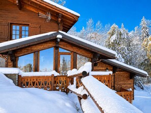 Una cabaña de madera con techo inclinado, ventanas grandes y un porche cubierto de nieve.