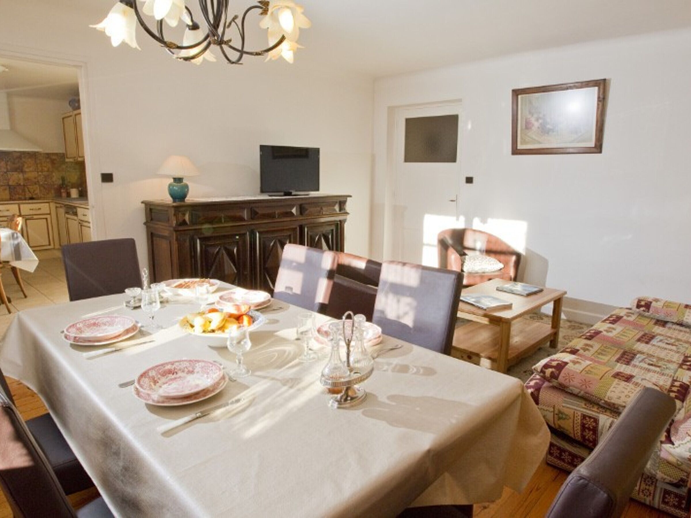 Zona pranzo con tavolo apparecchiato per quattro persone, una televisione e un divano.