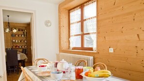 A dining area with a table set for four, wooden walls, a window with lace curtains, and a visible kitchen in the background. - Spacious 3-room apartment with Wi-Fi and parking in Saint-Chaffrey (Saint-Chaffrey)