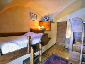 Ein Schlafzimmer mit einem Holzbett, einem Nachttisch mit Lampe, einer kleinen Ablage mit Blumen und einem Holzschrank.