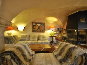 A cozy living room with a sofa, armchairs, a coffee table, a painting, and a bookshelf.