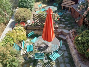 Eine Terrasse im Freien mit einem runden Tisch, blauen Stühlen und einem orangefarbenen Sonnenschirm.