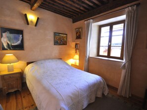 Ein Schlafzimmer mit einem Bett, Nachttischlampen, einem Fenster mit Vorhängen und Bildern an den Wänden.