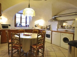A kitchen with a dining table, chairs, a chandelier, a microwave, a stove, a washing machine, and a sink.