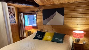 A wooden cabin room with a bed, two bedside lamps, a window with curtains, and a painting on the wall. - Spacious 6-Room Chalet for 10, Private Garden, Near Serre Chevalier Pistes (La Salle-les-Alpes)
