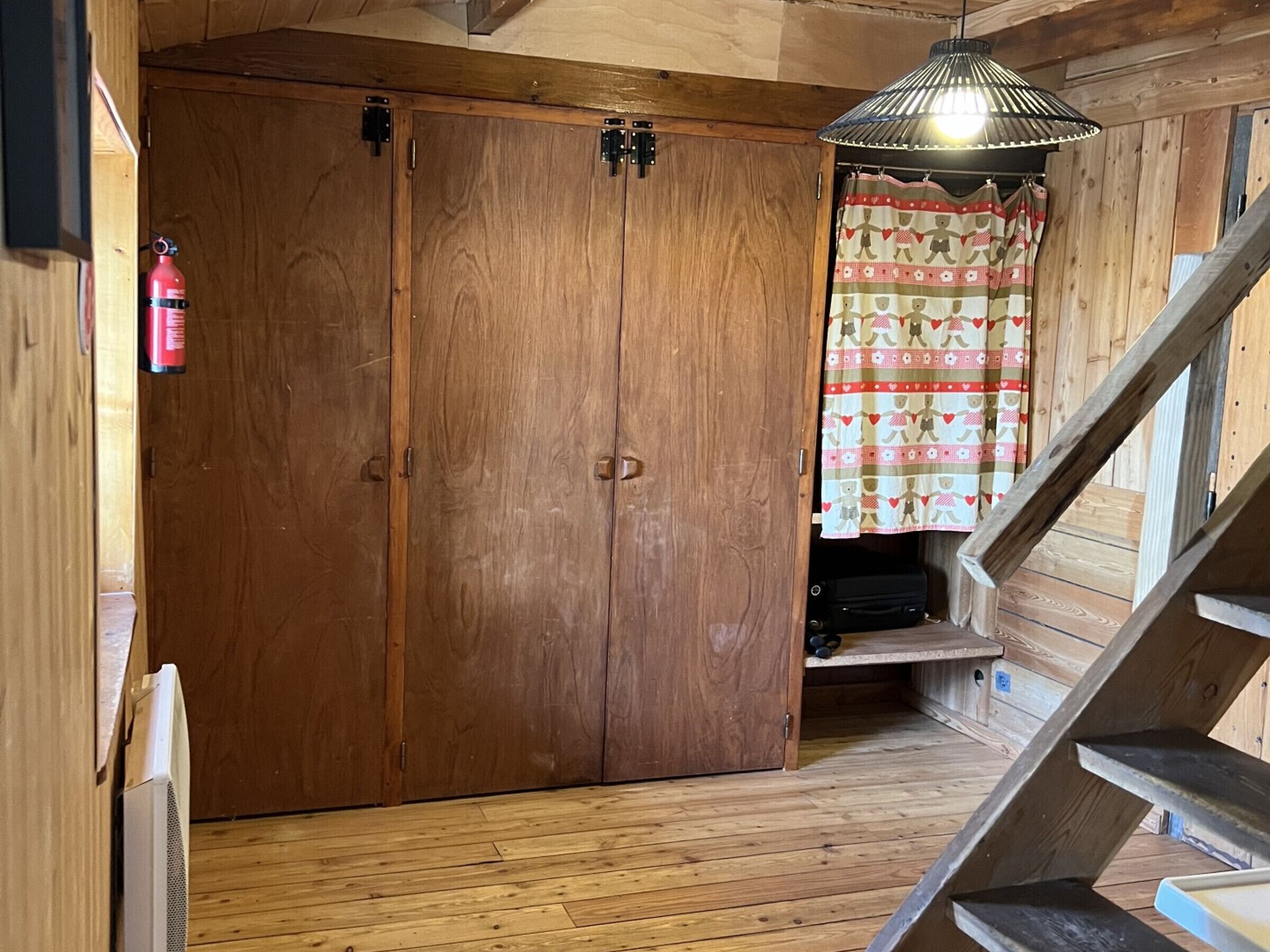 Une pièce en bois, avec une armoire, un luminaire suspendu et un rideau à motifs.