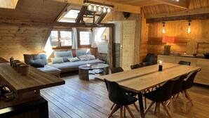 A cozy cabin interior with a wooden floor, a sofa, a dining table, and a kitchen area. - Spacious 6-Room Chalet for 10, Private Garden, Near Serre Chevalier Pistes (La Salle-les-Alpes)