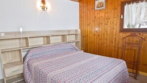Een slaapkamer met een houten hoofdbord, een bed met een decoratieve spreideken, een wandlamp en een raam met gordijnen.
