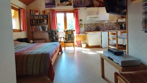 A cozy room with a bed, a bookshelf, a dining table, and a kitchen area.