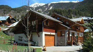 A wooden chalet with a stone facade, wooden balconies, and a mountain backdrop.