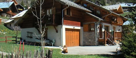 A wooden chalet with a stone facade, wooden balconies, and a mountain backdrop.