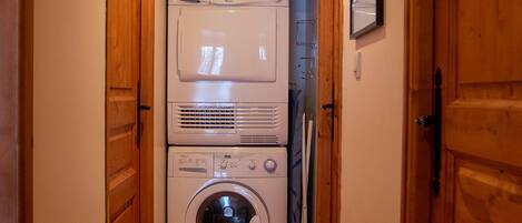 A laundry room with stacked washers and dryers, wooden doors, and a shelf with cleaning supplies.