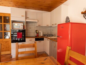 Une cuisine de taille modeste, avec des meubles blancs, un réfrigérateur rouge, un plancher en bois et un dosseret carrelé.
