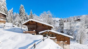Una cabaña de madera con balcón, rodeada de árboles cubiertos de nieve y un cielo azul despejado.