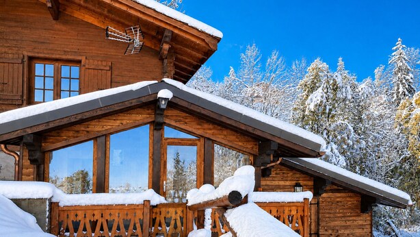 Una cabaña de madera con techo inclinado, ventanas grandes y un porche cubierto de nieve.