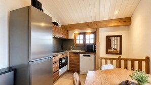 Una cocina moderna con un refrigerador de acero inoxidable, armarios de madera, un horno empotrado y un comedor con mesa y sillas de madera.