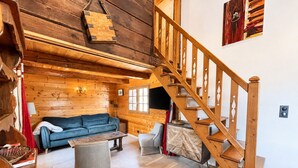 Un interior de madera con una escalera, un sofá, una mesa y una silla.