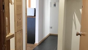 Un couloir étroit, avec une porte en bois sur la gauche et une porte blanche sur la droite.
