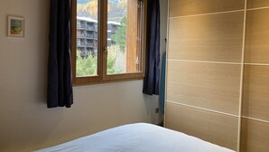 Une chambre à coucher avec un lit, une fenêtre avec des rideaux et une vue sur les bâtiments et les arbres à l’extérieur.