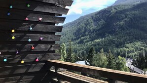 Une terrasse en bois, agrémentée d’ornements colorés suspendus, qui offre une vue sur un paysage montagneux boisé.