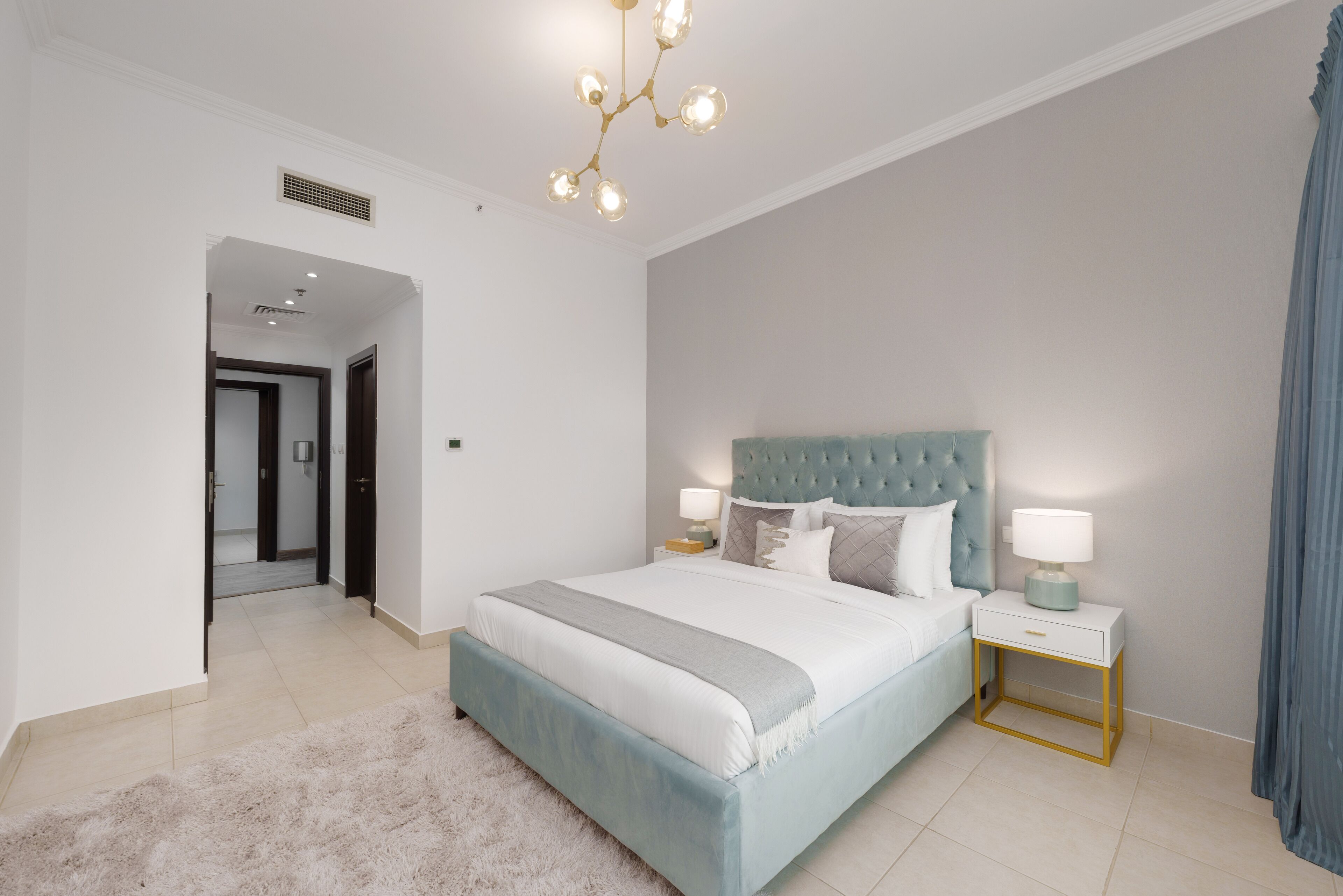Un dormitorio con una cama grande, cabecera capitonada, mesitas de noche con lámparas y una alfombra mullida.