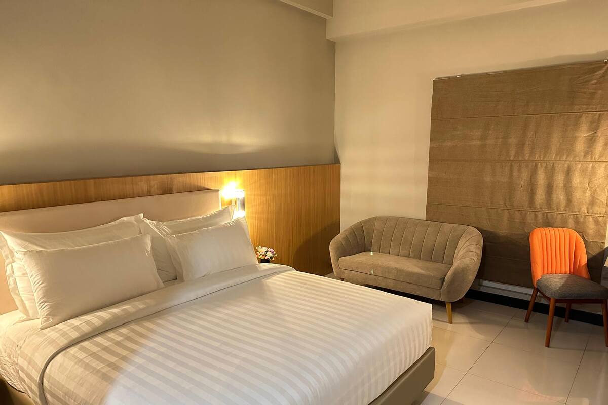Ein Hotelzimmer mit einem großen Bett, einer Couch, einem orangefarbenen Sessel und einem Nachttisch mit Lampe.