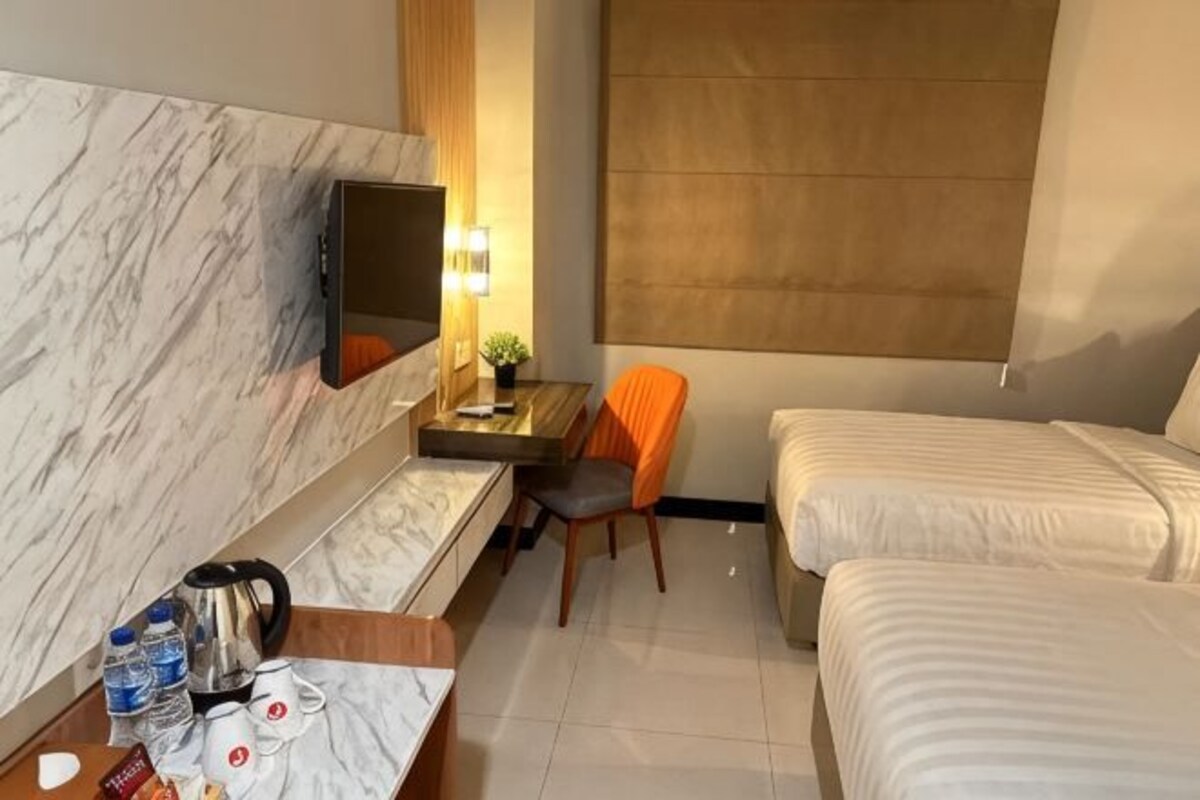 Hotelkamer met een marmeren wand, een televisie, een bureau met stoel, een bed en een raam met bruin zonnescherm.