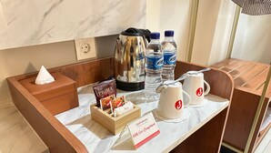 A hotel reception desk with a coffee maker, water bottles, a tissue box, and a sign promoting the hotel. - d'primahotel Jemursari Surabaya (Surabaya)