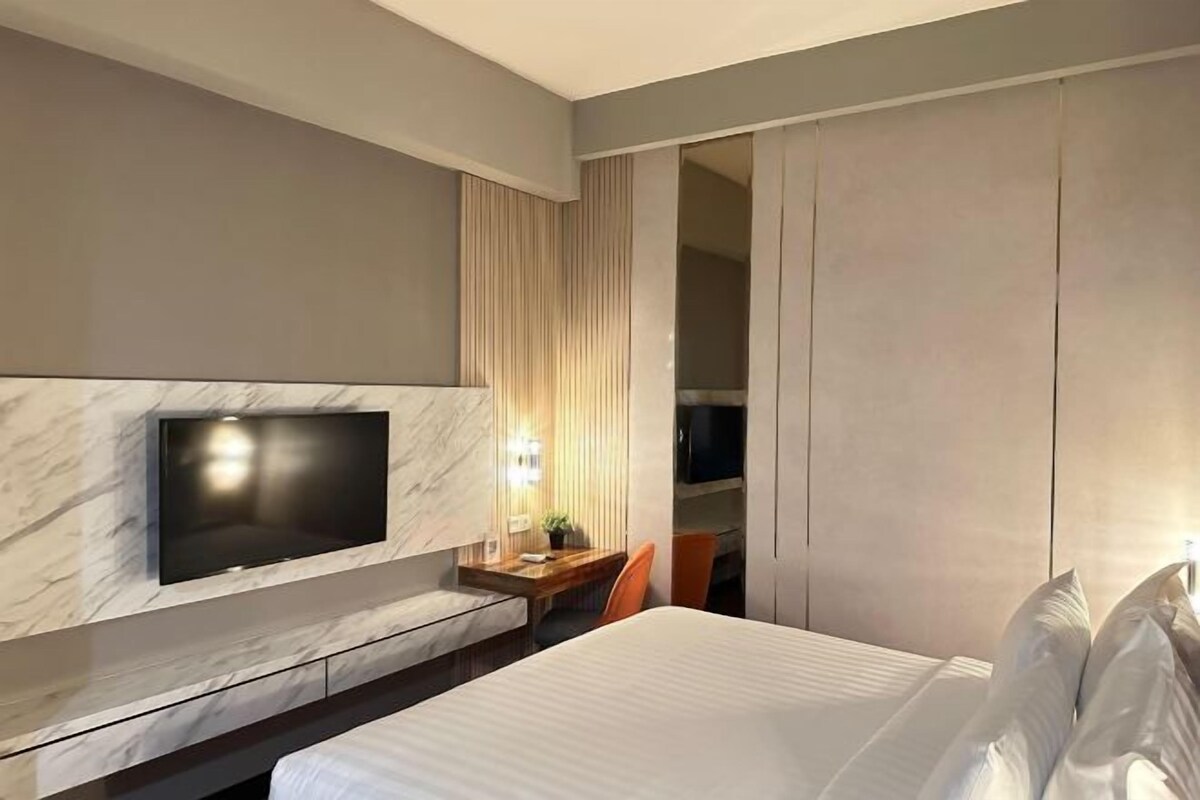 Ett modernt hotellrum med en stor säng, en platt-TV som är monterad på en vägg av marmor, ett skrivbord i trä och en skjutdörr till garderoben.