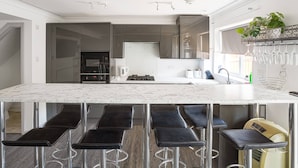 A modern kitchen with a marble countertop, black bar stools, and a built-in oven. - Get Away Home With Hot Tub Sleeps 6 (Peacehaven)