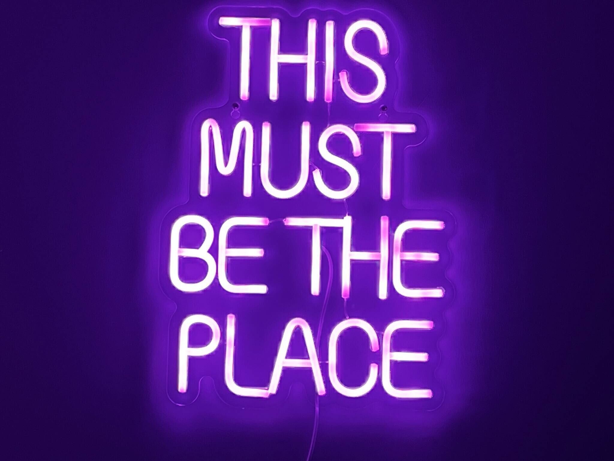 A neon sign with the text "THIS MUST BE THE PLACE" against a dark background.