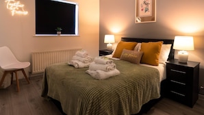 A neatly made bed with a green blanket, two bedside lamps, and a window with a view of the outside. - Get Away Home With Hot Tub Sleeps 6 (Peacehaven)